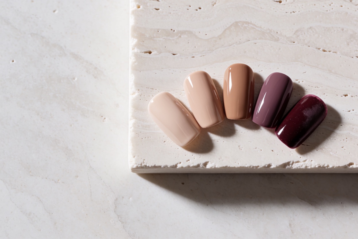 Gel polish swatch tips fanned on a stone slab, gloss fading from fresh to worn